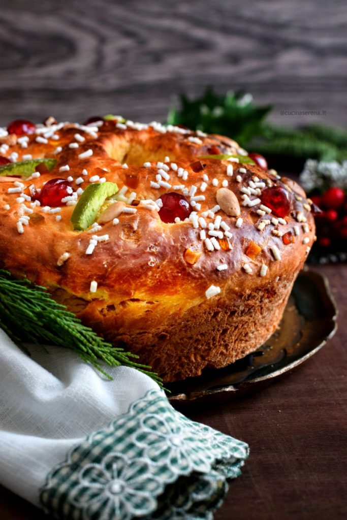 dolce dell'epifania spagnolo ciambella con frutta candita mandorle e granelle di zucchero messa su un vassoio appoggiato au un tavolo, intorno decorazioni di rami di abete e foglie di vischio