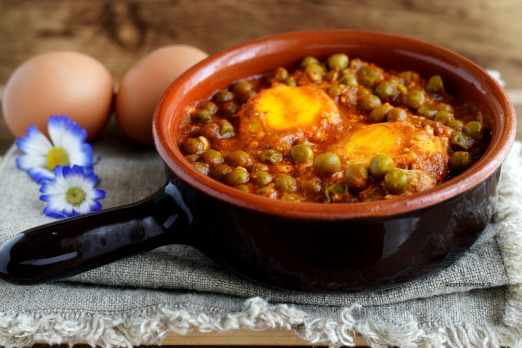 Uova con pisello al sugo è una ricetta facile e veloce con le uova e i legumi. La foto rappresenta un tegamino di coccio con manico nel quale ci sono le uova cotte immerse nei piselli al sugo