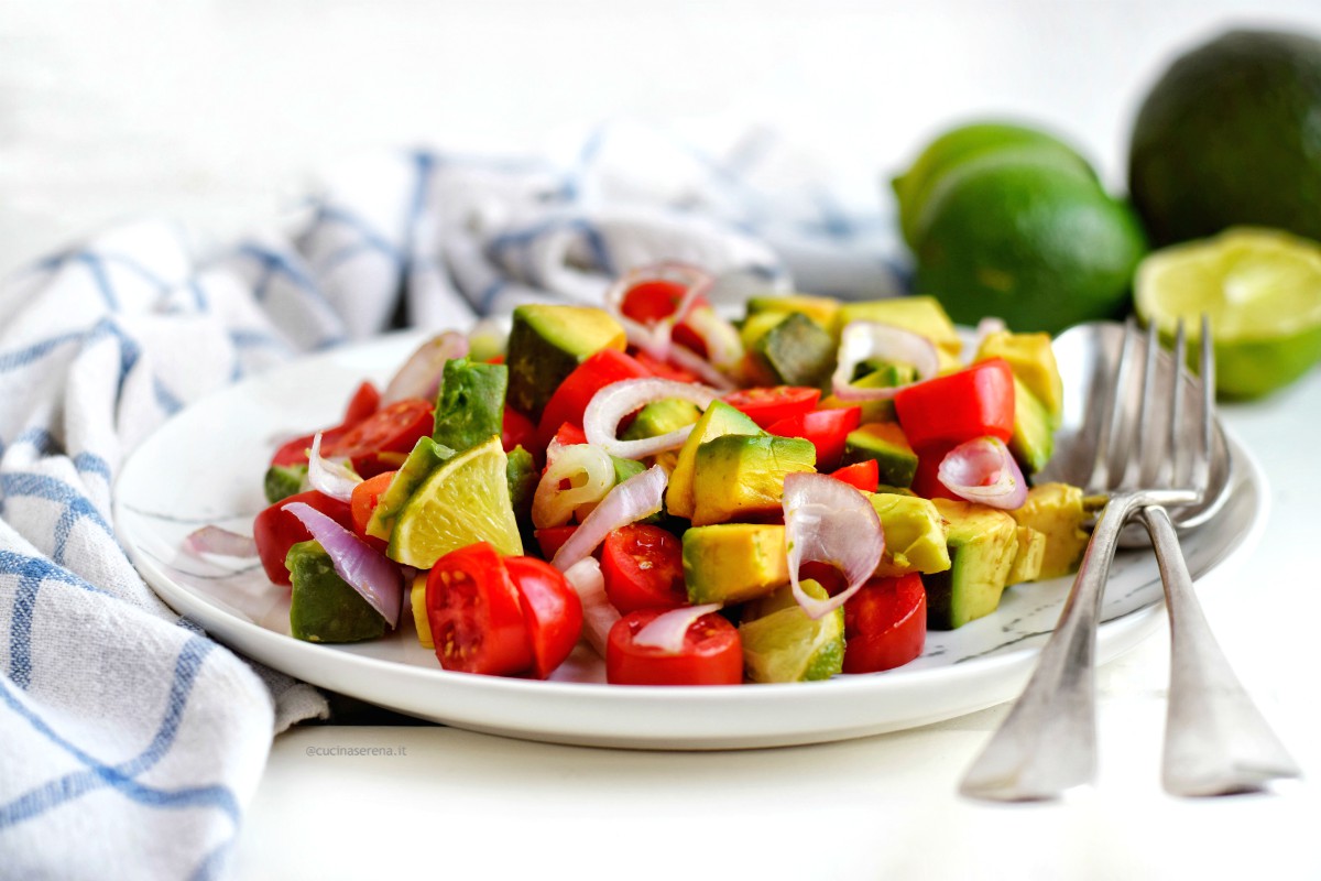 Insalata guacamole servits su un piatto marmorizzato accanto un canovaccio a scacchi bianco e blu sullo sfondo lime ad avocado