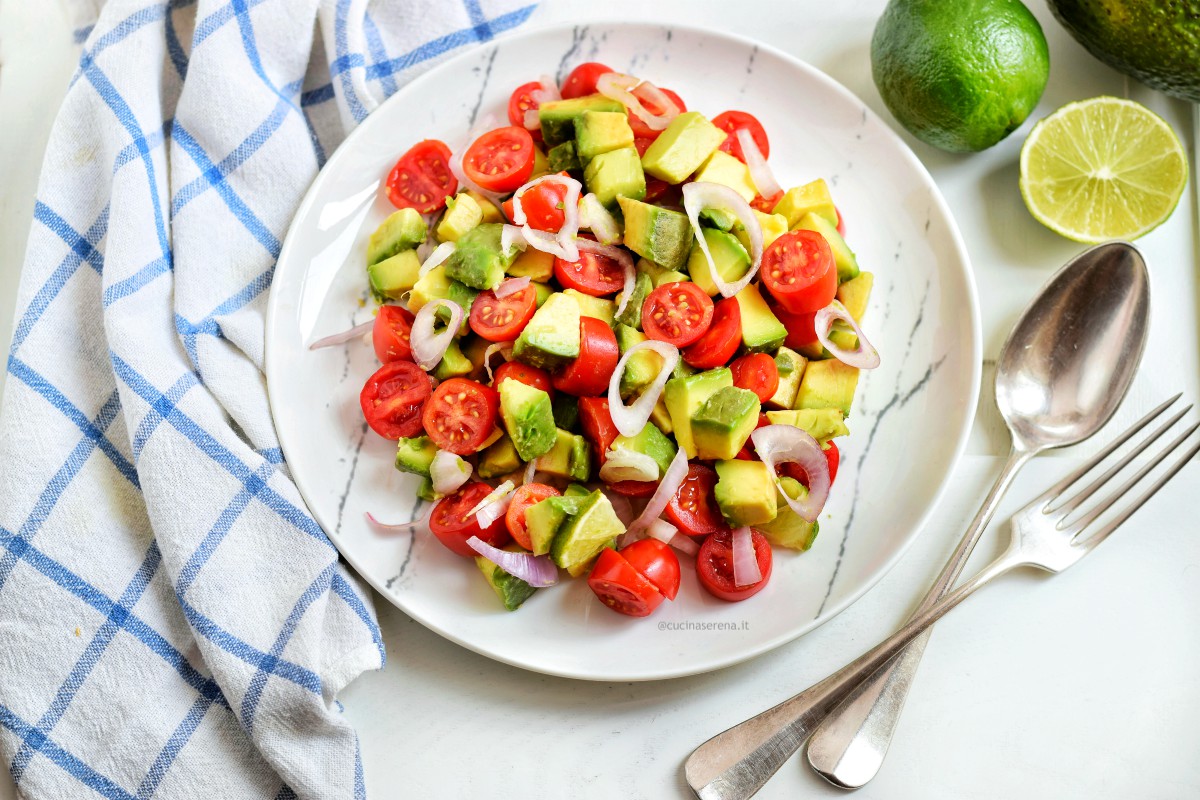 Insalata guacamole servita in un piatto marmorizzato con accanto un canovaccio  a quadrettoni bianco e azzurro. Foto zenitale attorno avocado e lime 