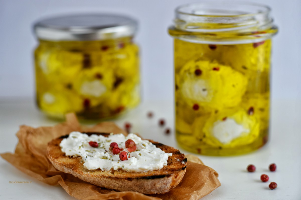 Labneh formaggio libanese fatto con yogurt filtrato, in questa foto ridotto in palline e messo nei barattoletti con spezie e pepe rosa in grani. di lato una fetta di pane con il formaggio spalmato