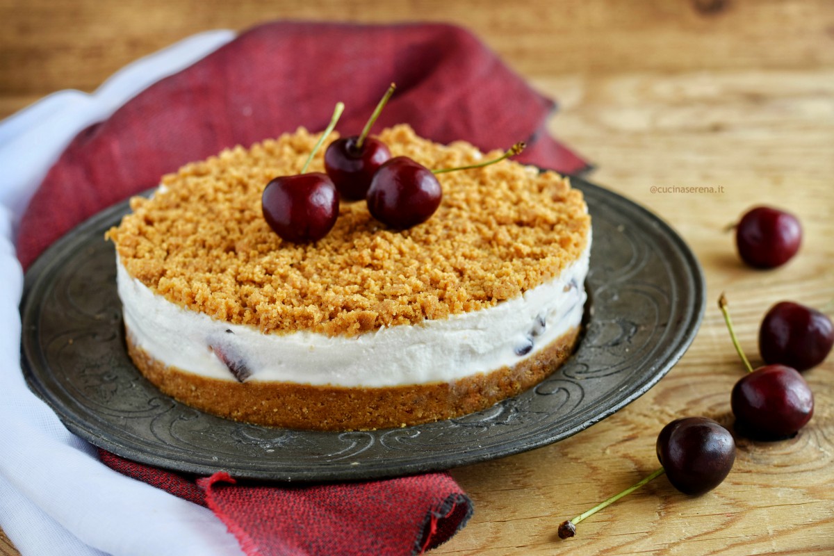 briciolata fredda senza cottura in forno fatta con ricotta panna e ciliegie a pezzi. Nella foto presentata su un vassoio di peltro adagiato sopra due stoffe una rossa e una bianca di tela