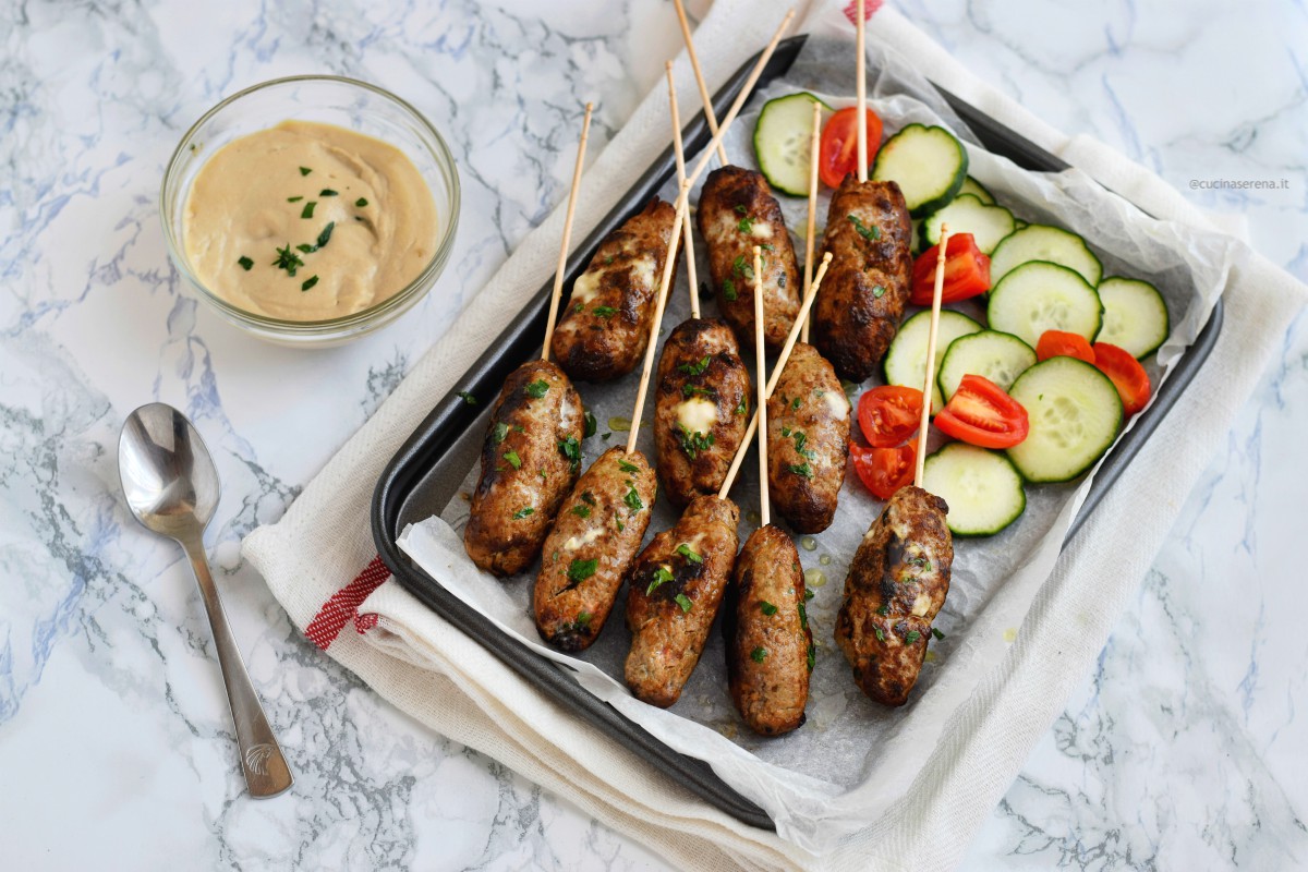 Kofta polpette di carne medio orientali con carne macinate e spezie nella foto servita nella versione  kofta meshweya come spiedini in una teglia con salsa tahini in accompagnamento