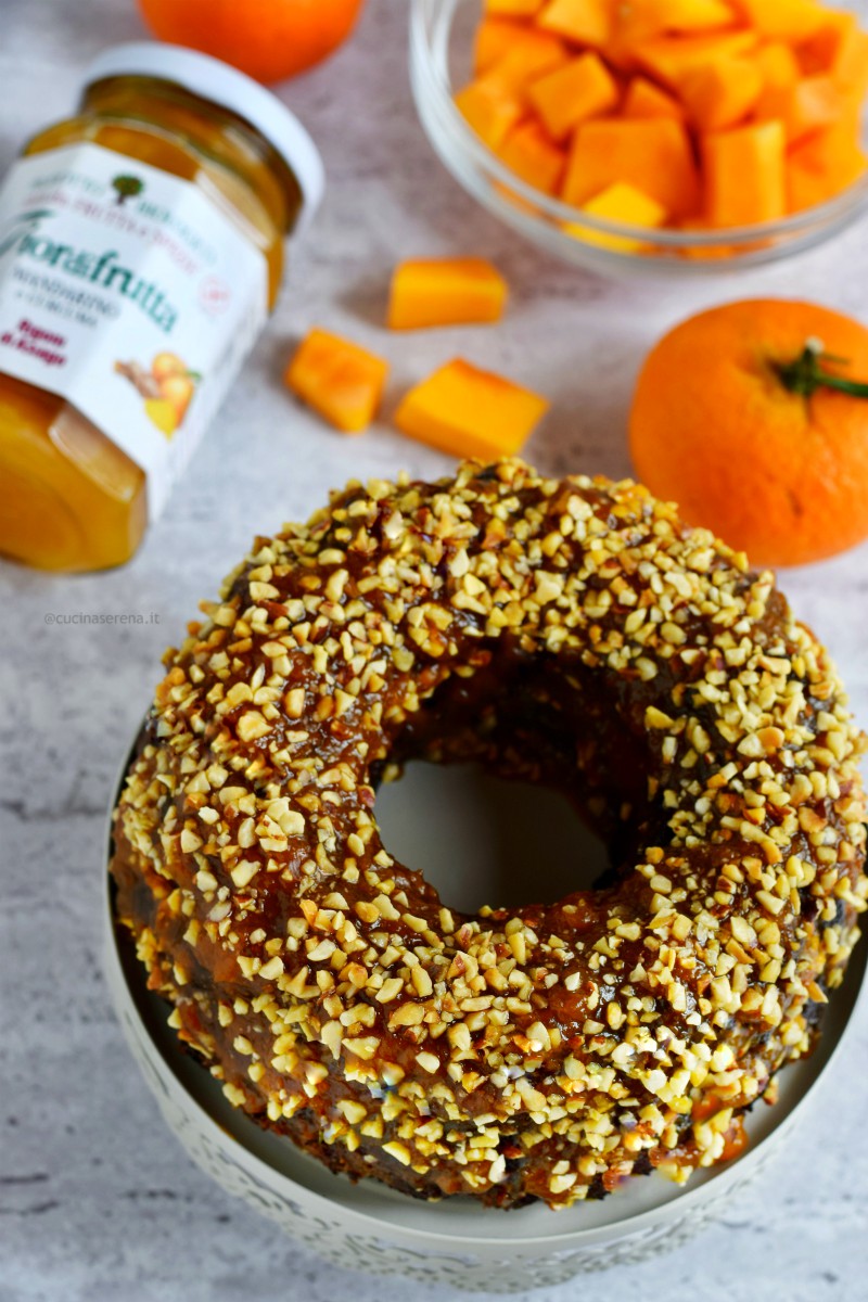 Torta alla zucca e mandarino con curcuma gluten free. Nella foto zenitale il dolce è adagiato su una alzatina per dolci e sullo sfondo si intravedono mandarini e zucca a cubetti