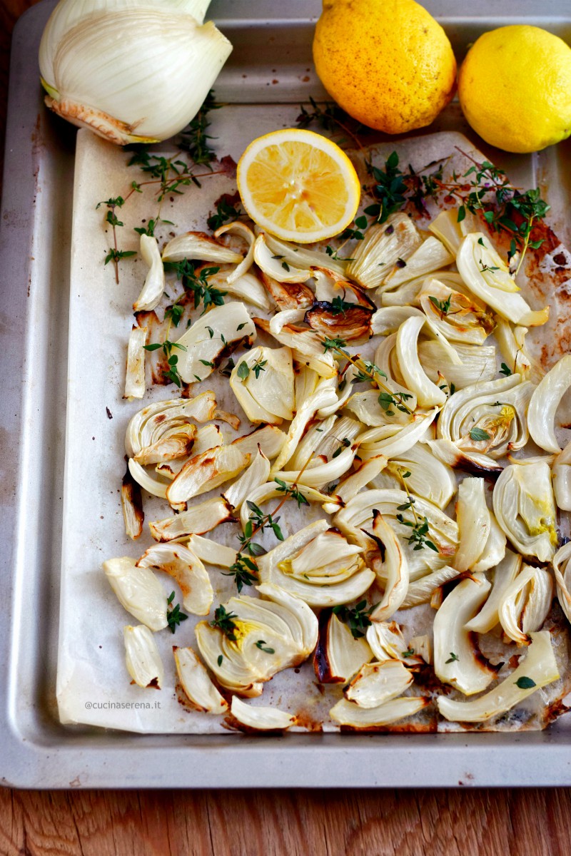 Finocchi al limone e timo cotti al forno, nella foto presentati nella teglia nelle quale sono stati cotti con limoni, rametti di timo e un finocchio intero vicini per richiamare gli ingredienti della ricetta