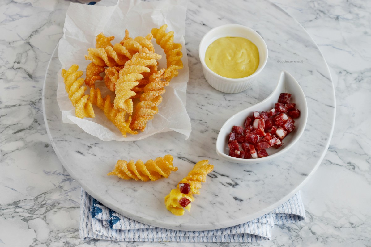 Carbonara con pasta soffiata servita su un vassoio di marmo, la pasta fritta è messa su carta forno, accano una citolina con la crema di parmigiano e uovo, un'altra ciotola con spianata romana Clai