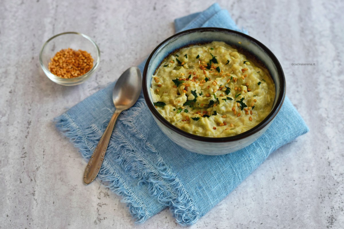 Babaganoush o caviale di melanzane crema di melanzane nella foto presentata in una ciotolina di ceramica deposta su un tovagliolo celeste di lino, accanto una piccola ciotola con semi di sesamo che richiamano la salsa tahini con quale viene fatta questa salsa,