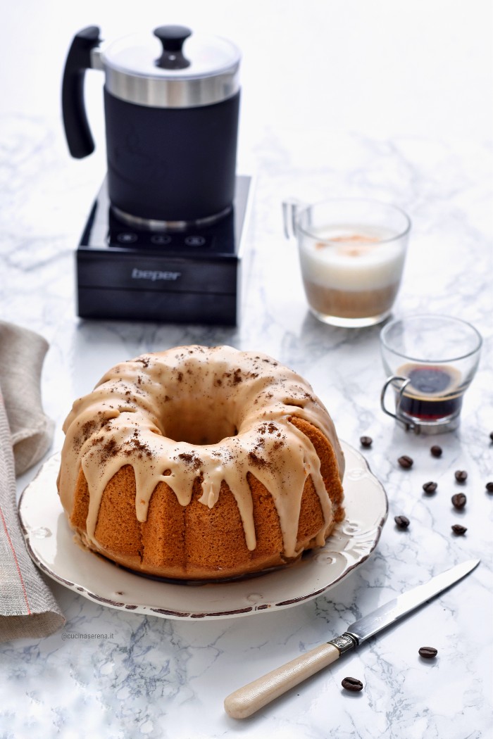 Torta al cappuccino bundt cake con glassa al caffè su un piatto vicino, caffè, cappuccino e schiumalatte Beper per fare il cappuccino